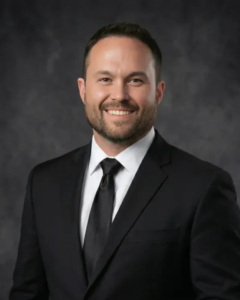 Gerardo Mena smiling, in a black suit and tie